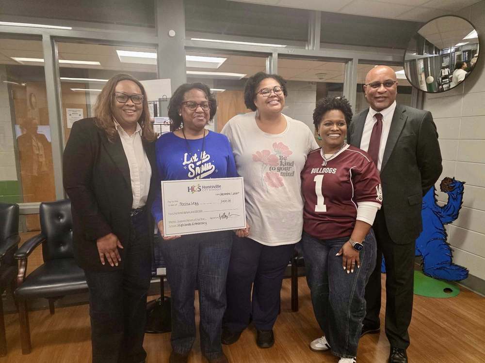 Ms. Legg smiles while holding a large ceremonial check, standing alongside administrators who are also smiling for the photo.