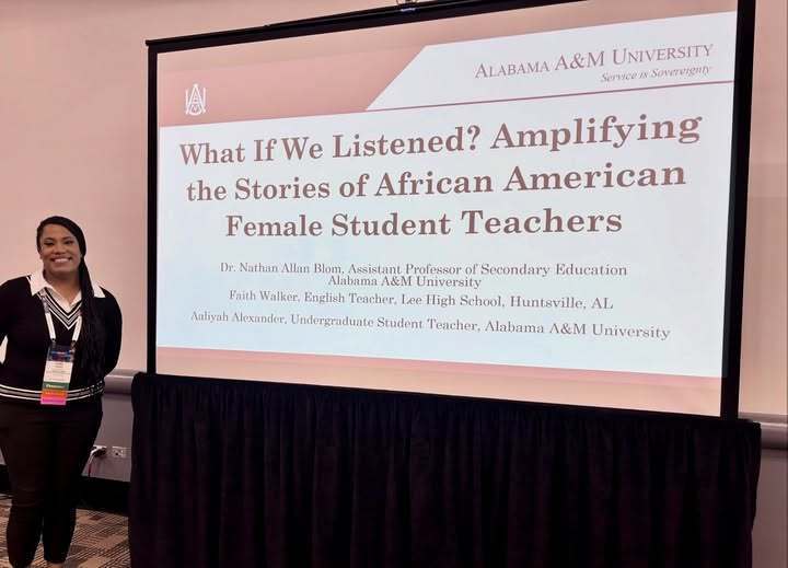 Ms. Walker, an English teacher at Lee High School, stands smiling beside a large presentation screen at a conference. The screen displays her session title, “What If We Listened? Amplifying the Stories of African American Female Student Teachers,” along with the names and affiliations of the presenters, including Alabama A&M University and Lee High School.