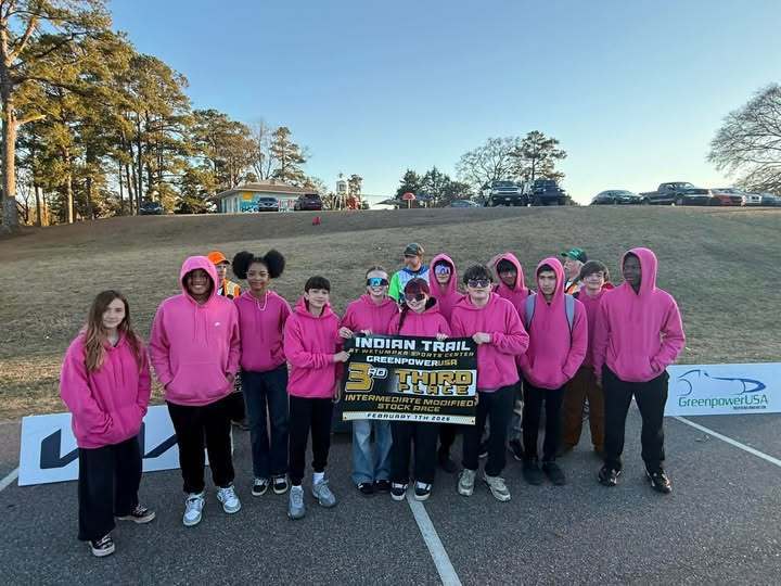 students in pink sweatshirts at a race holding a sign for greenpower
