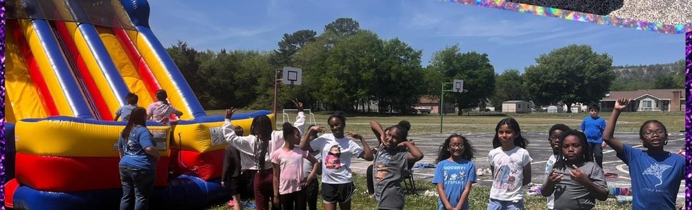 A large inflatable slide is in a field with a group of students lined up , waiting to use it.