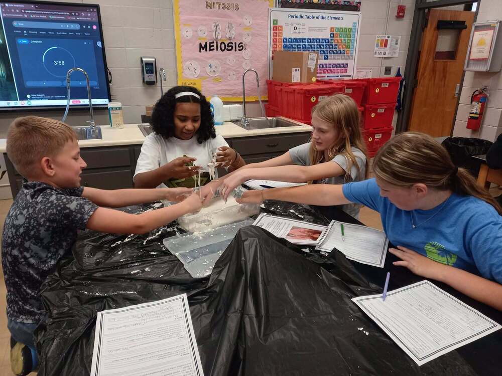 6th grade science students at a center exploring oobleck, a gooey, white substance.