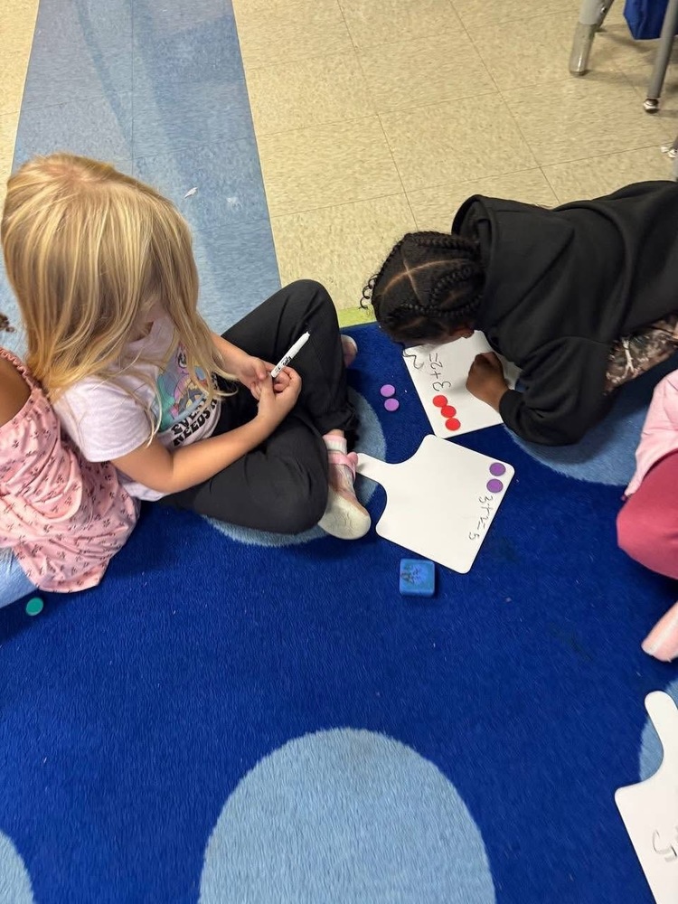 2 students on the carpet with white board and red and purple counters on top of the white board