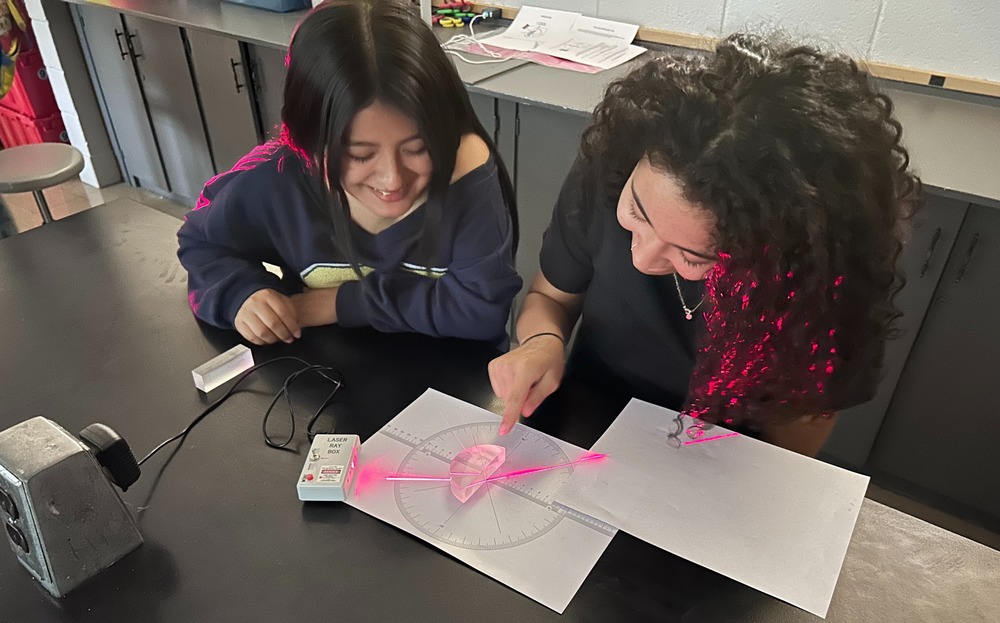 two students looking at pink light refract through glass