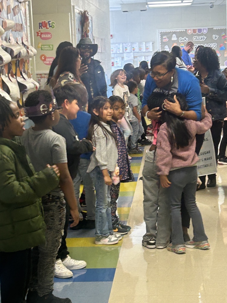 Mrs. Woods walks through the hall hugging students as other students and staff look on.