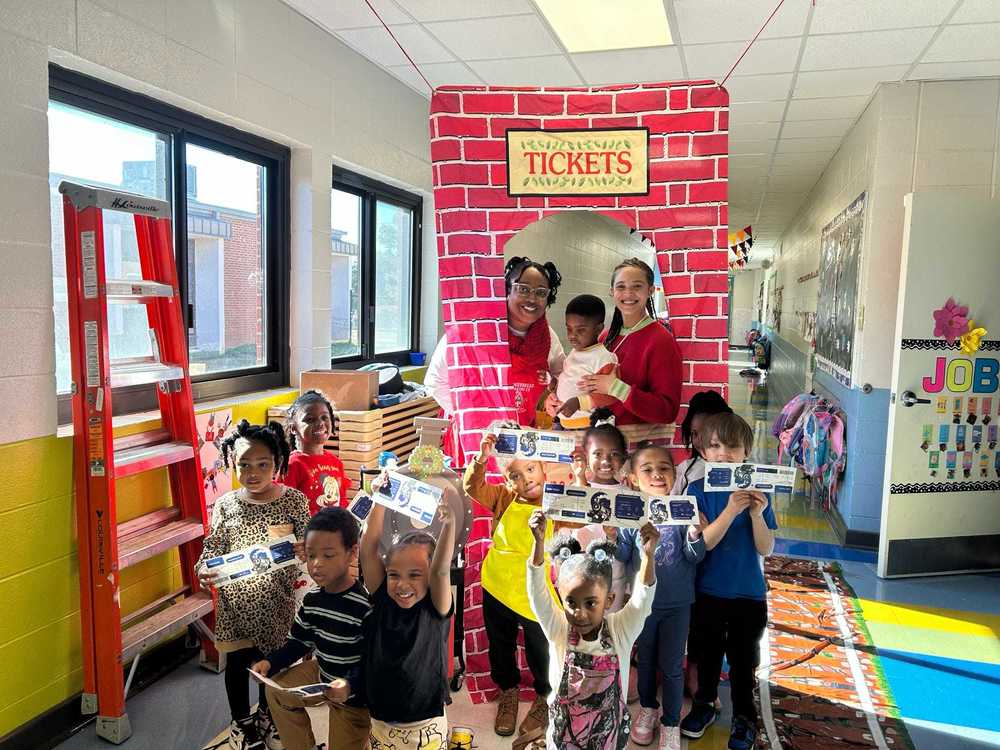 Pre-K students holding Polar Express tickets and smiling in front of a festive train-themed display at school.