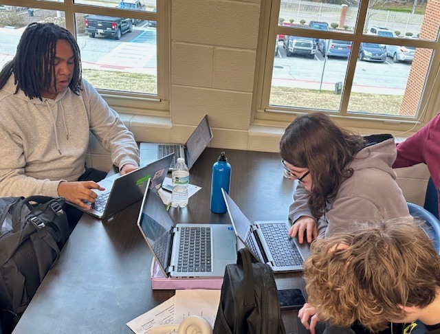 3 students work together on laptops writing code.