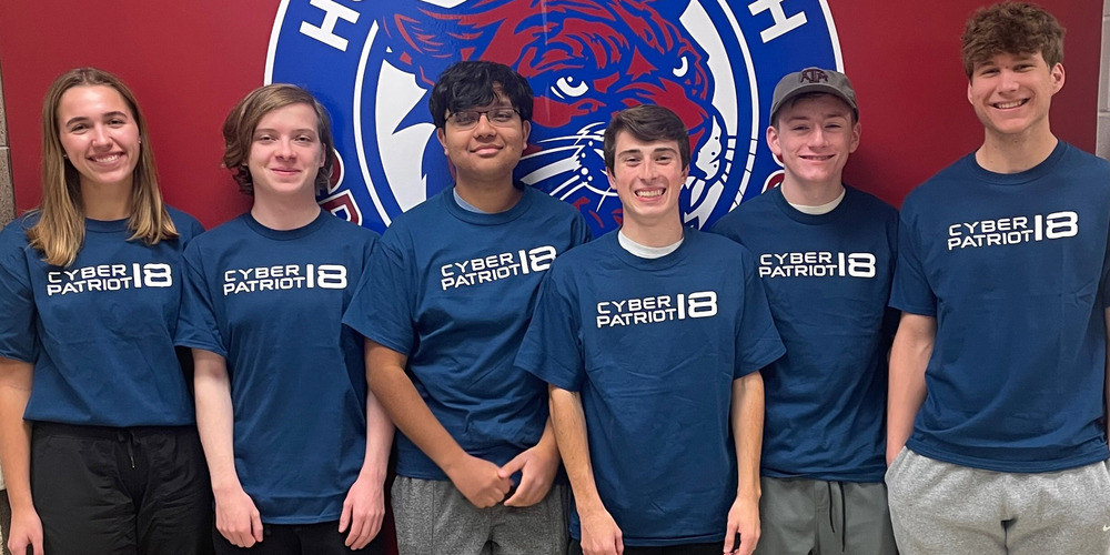 Huntsville High School Cybersecurity Team pose in front of a red wall bearing the school logo