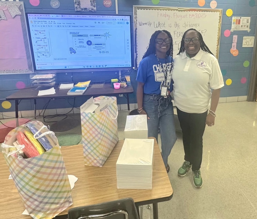 Ms. Tate poses in her art classroom with a representative presenting a generous donation from Dailonna Dozier Help Foundation.
