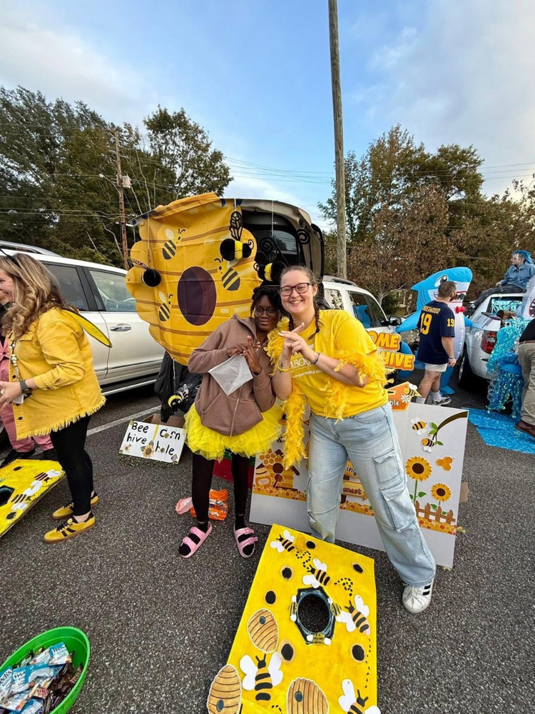 Ms. McBride posing for a picture with a student in front of the yellow house trunk at trunk or treat