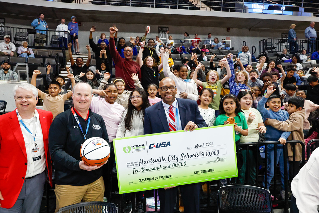 Dr. Sutton poses with Conference USA personnel, HCS staff, and elementary students while showing the game ball and $10,000 grant check.
