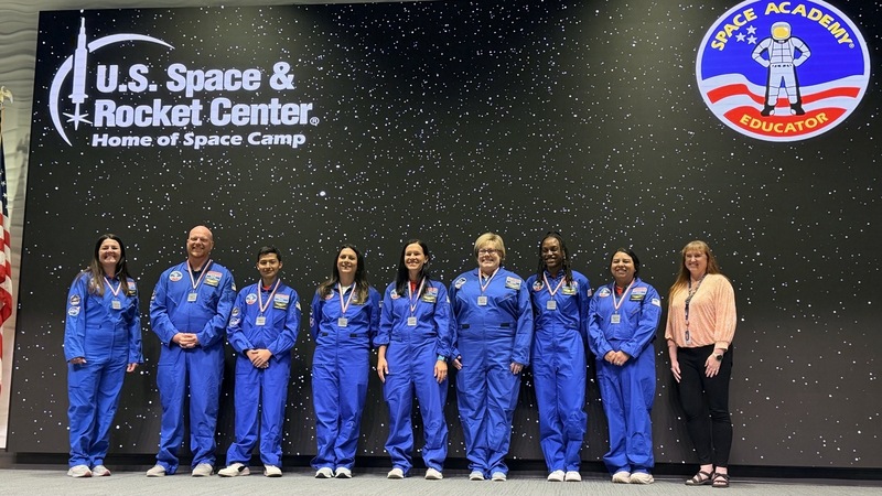 HCS Educators post in front of the large U.S. Space & Rocket Center black and stars wall