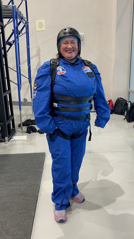 Teacher wearing blue space camp suit and helmet, preparing to go on a simulation experience