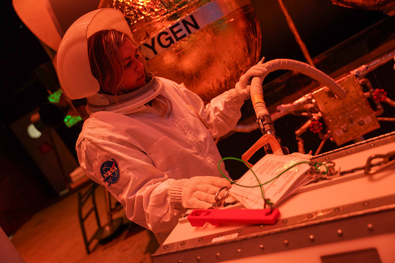Teacher in astronaut suit working hoses and levers in simulated environment