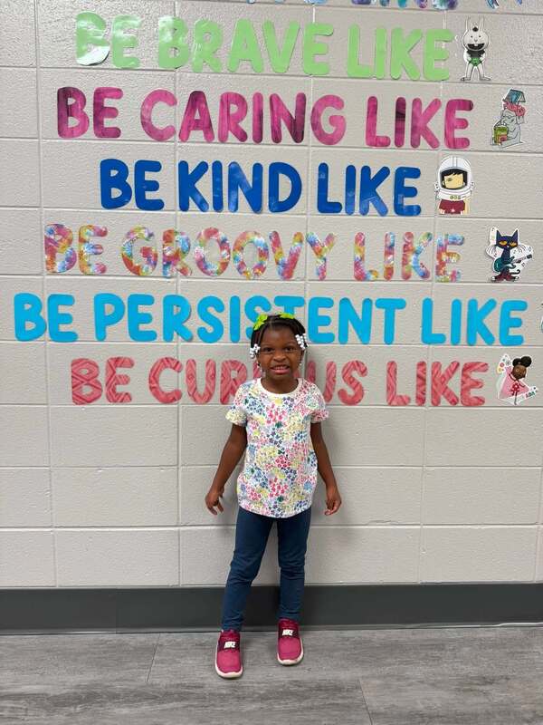 Our Pre-K student of the Month, standing in front of library decorations