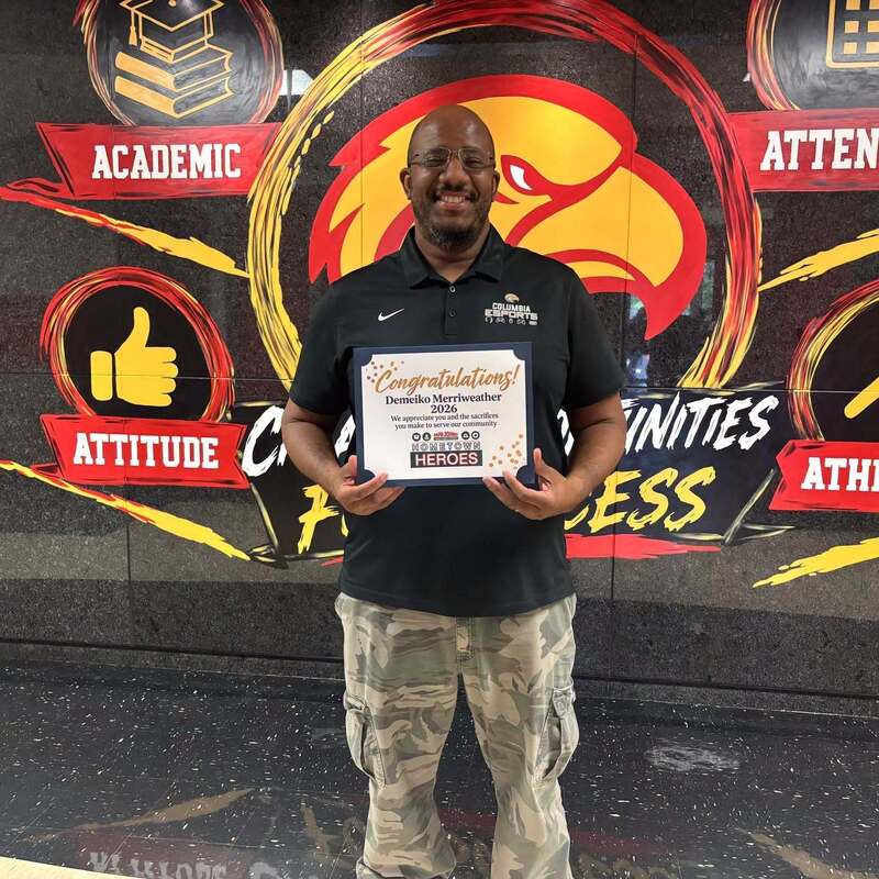Mr. Merriweather standing in front hall with Columbia sign on black marble wall posing with a certificate in his hand