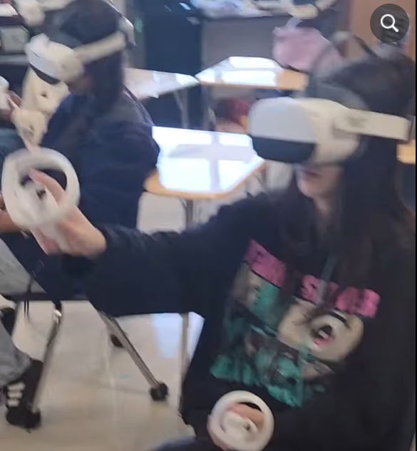 Two girls use the wands to "handle" virtual items. They're wearing white headsets.