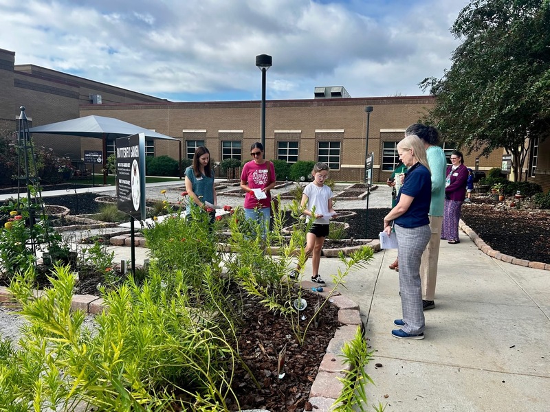 A Student in the Outdoor Classroom presenting about the pollinator garden to 5 adult visitors.