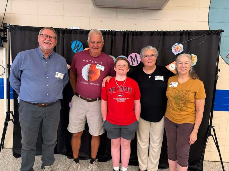Student standing with four adults in front of photo backdrop that says welcome