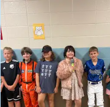 5 students dressed as a soccer player, an astronaut, a coach, a singer and a baseball player for college and career week . standing in the hall under a yellow paper with an owl in it.