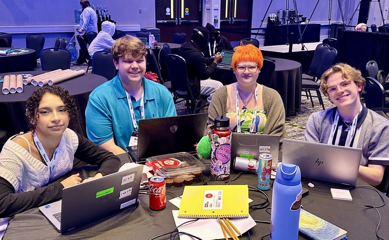 Four students pose for a photo with their laptops at the Cyber Summit