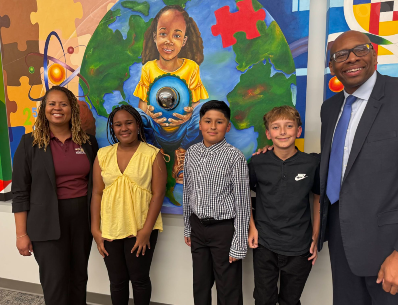 AP Stallworth-Brown and Superintendent Dr. Sutton pose with our pledgers (an African-American girl, a Hispanic Boy and a Caucasian Boy) in front of a colorful mural.