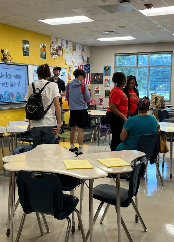 A student shows his parents his desk in Mrs. Parrish's room as Mrs. Parrish talks with Mrs. Elike and another parent.