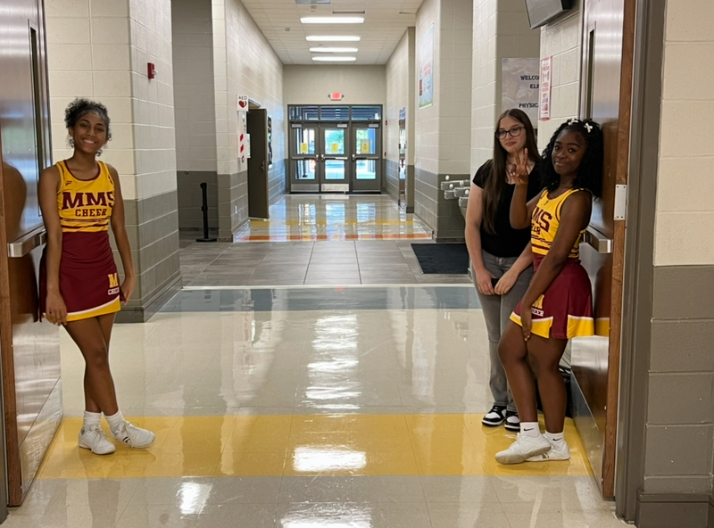 Two cheerleaders dressed in gold and crimson uniforms flank a doorway greeting guests.