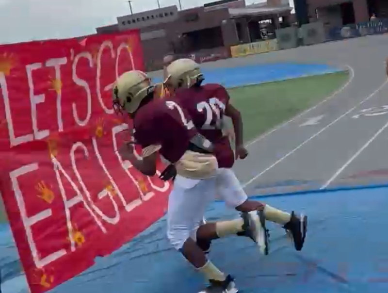 Two football players head toward a large "Let's Go  Eagles" sign