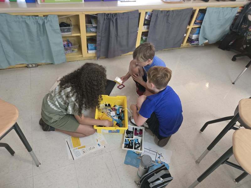 students sitting in floor looking at a yellow box full of legos