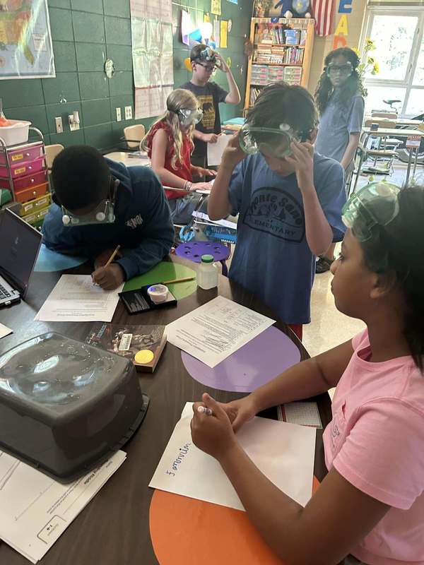 students sitting at with lab sheet wearing goggles