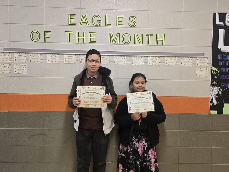 Two students stand in front of a sign that says  "Eagles of the month"