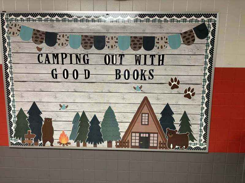 Bulletin Board with a cabin, trees, and the words Camping Out With Good Books