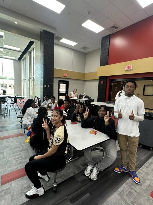 Students sitting  and one standing at a table in the cafeteria during the Perfect Attendance Celebration