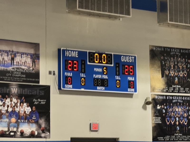 A blue scoreboard reading "Home (McNair) 23 and Guest (MMS) 25)