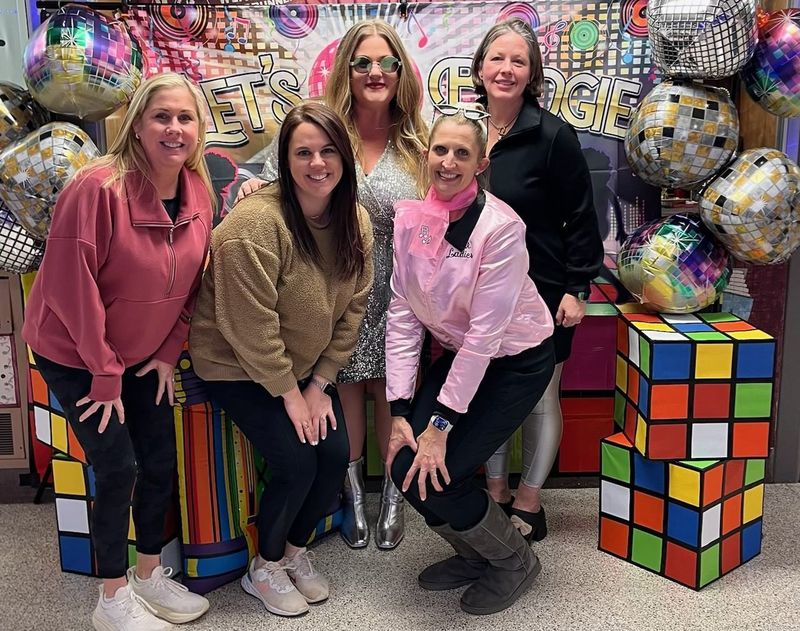 Weatherly PTA  pose in front of a colorful disco-themed background with Rubik's cubes and disco balls.