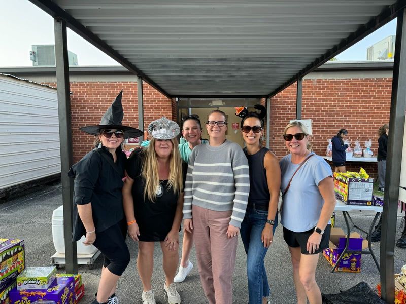 Weatherly PTA pose together under a covered walkway in front of a brick building, some wearing festive hats.