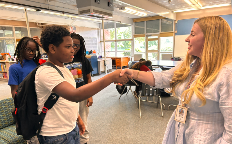 In the library, one of the "Sharks" is shaking hands with a student as they make a deal for an investment on the presented invention.