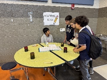 Students standing around a yellow table with a sign that says "Academic Team"