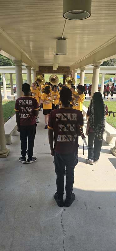 The band students in black and gold with instruments standing in the breezeway to enter the school