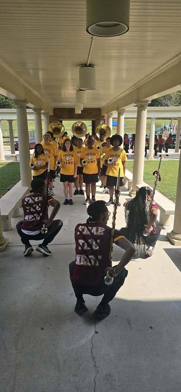 The band students stooping in black and gold with instruments standing in the breezeway to enter the school