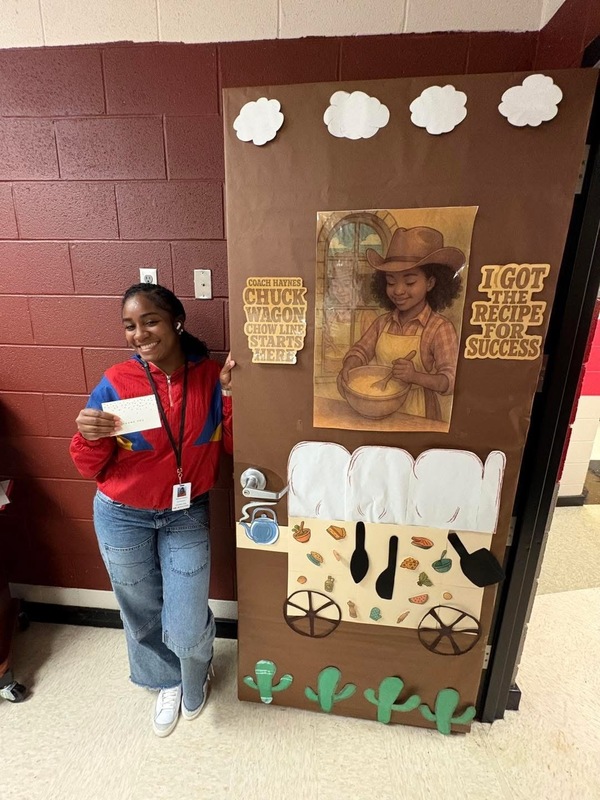 Ms. Haynes standing in front of her door decorated with a food wagon, girl stirring in bowl