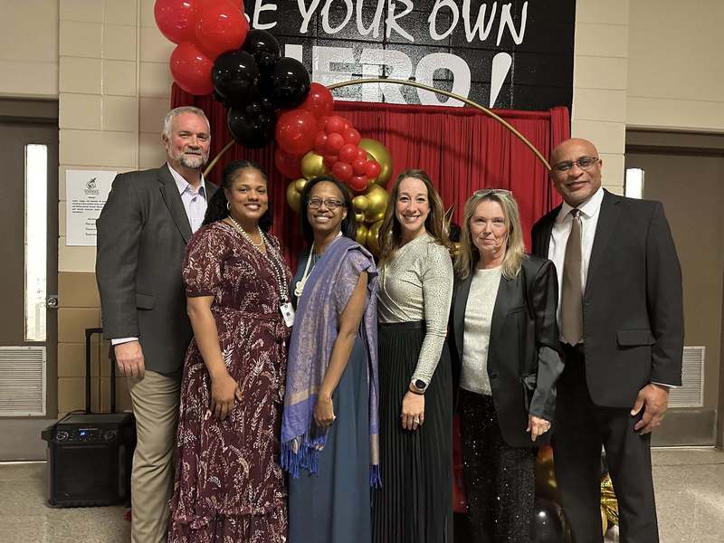 Members from central office with Principal Sutton in front of a our special backdrop with a balloon arch.
