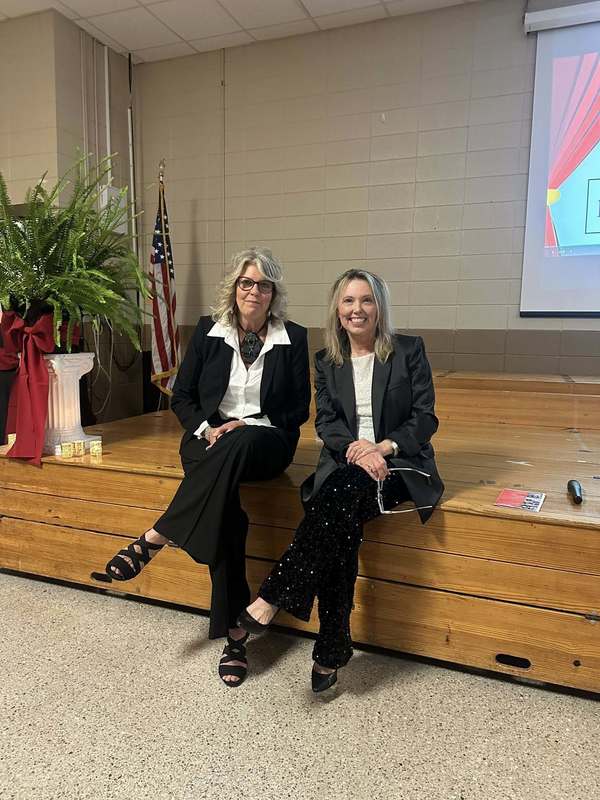 The principal and assistant principal, Ms. Sutton and Ms. Boisell sitting on the stage.