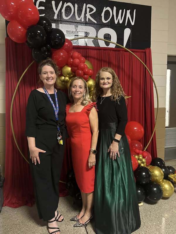 Our nurse, EL teacher, and counselor in front of the red backdrop.
