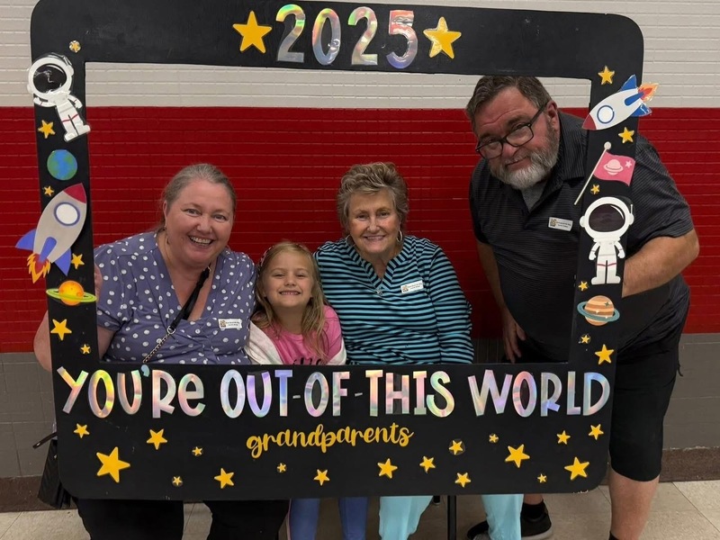 Four smiling people pose behind a space-themed frame with the text You're Out of This World. Grandparents 2025