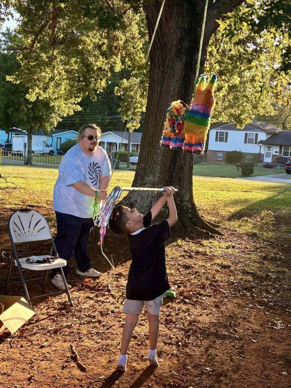 A student hitting the pinata while Mr. Whetstone holds the rope.