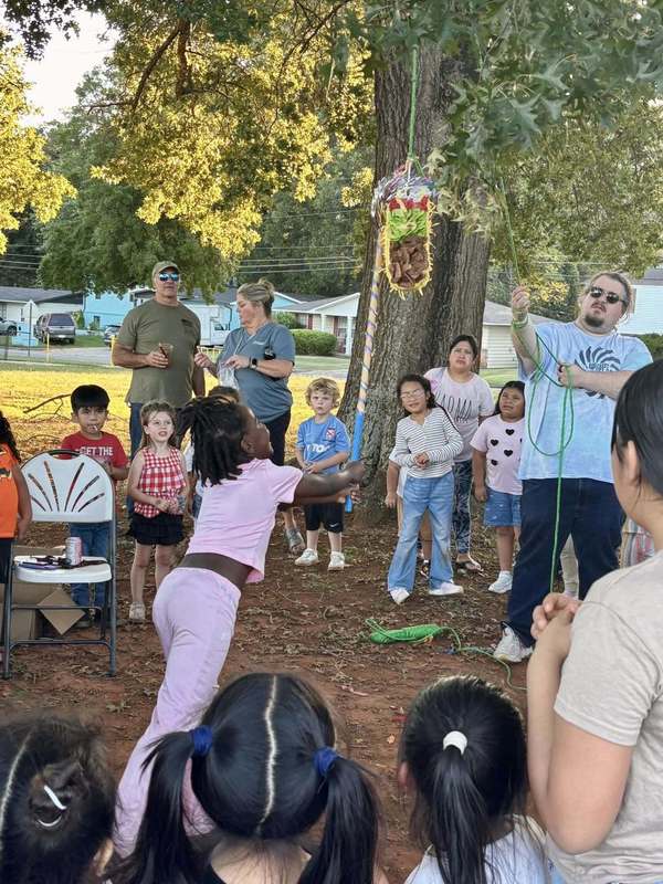 Student attempting to break the taco pinata while Mr. Whetstone holds the rope. Families stand by to grab candy.