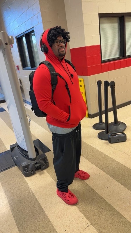 The principal of Columbia posing in red hodie , black bookbag, gray shirt hanging under hoodie with black joggers and red shoes on