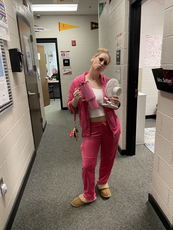  Counselor posing wearing pink jogging suit holding  up a pink cup in right hand and white fan  in right wearing brown house shoes 