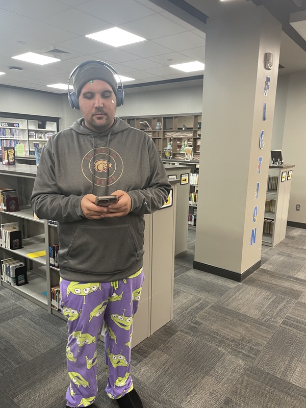 The Spanish teacher dressed in a gray hoodie with purple and yellow  pajama pants with a gray hat on his head with his cell phone in hand